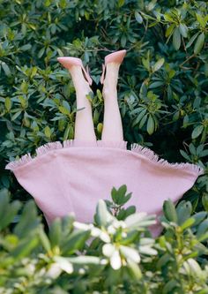 a woman laying on top of a pink blanket in the middle of some bushes and trees