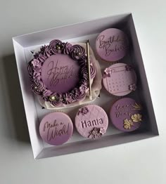 a box filled with lots of purple decorated cookies next to a cupcake in the shape of a wreath