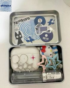 two tins filled with toys and magnets on top of a white table next to each other