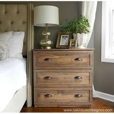 a bedroom with a bed, nightstand and lamp on it's side table in front of a window