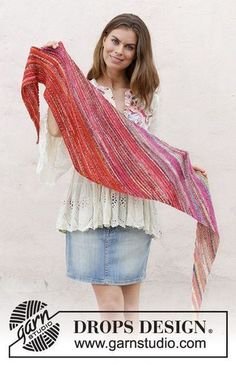 a woman holding up a multicolored shawl in front of a white wall