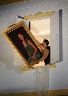 a man looking at a painting hanging on the wall in front of a window with white shutters