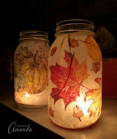 two mason jars with autumn leaves painted on the lids, one is lit and the other has a candle in it