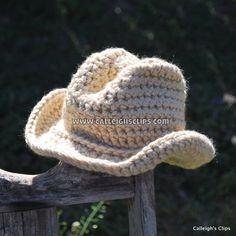 a crocheted cowboy hat sitting on top of a wooden bench in front of some bushes