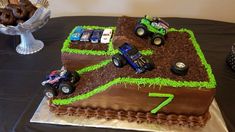 a birthday cake made to look like a dirt track with monster trucks on the side