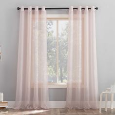 a window with sheer curtains hanging from it's sides and a wooden floor in front of