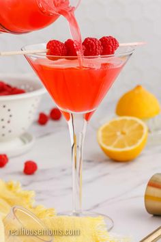 someone pouring raspberry lemonade into a martini glass with fresh raspberries in it