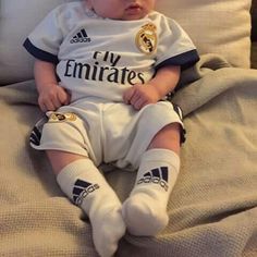 a baby sitting on top of a bed next to a white pillow with the word my emirates written on it