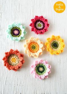 four crocheted flowers sitting on top of a white table next to each other