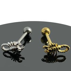 two pairs of gold and silver piercings on a black surface with reflection in the middle