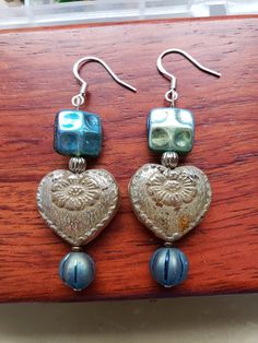 Heart-shaped drop earrings handmade from Czech glass beads with sterling silver ear wires. Heart shaped bead has a frosted coating, but is translucent amber in the light. Top square bead is shimmering blue/green, and a blue pumpkin bead at the bottom. Silver Beaded Heart Earrings Gift, Blue Heart-shaped Earrings With Ear Wire, Blue Heart Bead Earrings, Blue Nickel-free Sterling Silver Heart Earrings, Blue Heart-shaped Earrings With Heart Beads, Blue Sterling Silver Nickel-free Heart Earrings, Blue Sterling Silver Heart Dangle Earrings, Blue Heart Earrings, Blue Pumpkin