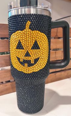 a black and yellow cup with a pumpkin face on the front is sitting on a table