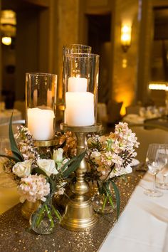 three candles are lit on top of a table with flowers and greenery in vases