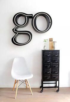 a white chair sitting in front of a black clock on the wall next to a dresser