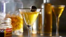 two glasses filled with yellow liquid sitting on top of a table next to bottles and jars