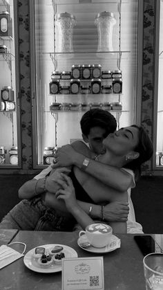 black and white photograph of two people hugging each other at a table with pastries on it