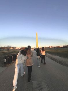 three people are walking down the road in front of a large yellow obelisk