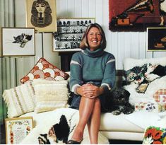 a woman sitting on top of a white couch next to many pillows and rugs