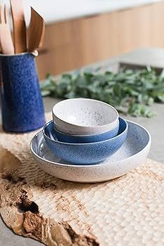 three blue and white plates stacked on top of each other next to a vase filled with greenery