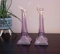 two pink glass candlesticks sitting on top of a table next to a potted plant