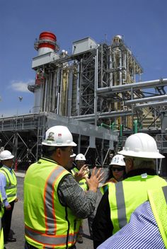 some people wearing hard hats and vests talking to each other in front of an oil refinery