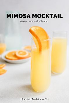 two glasses filled with orange juice on top of a white table next to sliced oranges