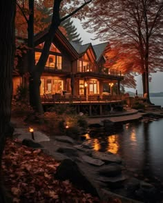 a house is lit up at night on the water's edge with trees surrounding it