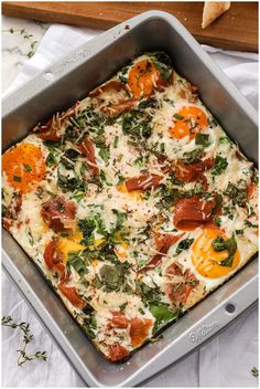 a square casserole dish with tomatoes, spinach and eggs in it on a white tablecloth