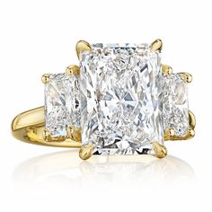 an engagement ring with three princess cut diamonds on the shoulders and sides, set in yellow gold