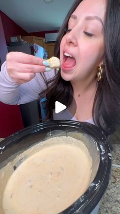 a woman eating food out of a crock pot with her mouth open and tongue out