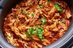 a slow cooker filled with shredded meat and garnished with cilantro