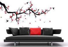 a black couch sitting under a red flowered tree wall decal on a white wall