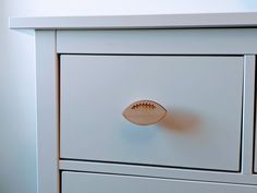 a white dresser with a football drawer knob on it's front and bottom drawers