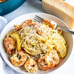 a white plate topped with pasta and shrimp next to a slice of bread on top of a table