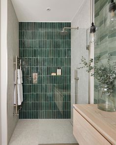 a bathroom with green tiles on the shower wall and wooden countertop, along with a plant in a glass vase