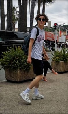 a man walking down the street with his foot in the air while wearing sunglasses and carrying a backpack