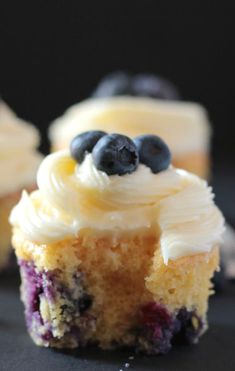 two cupcakes with white frosting and blueberries on top are sitting on a black surface