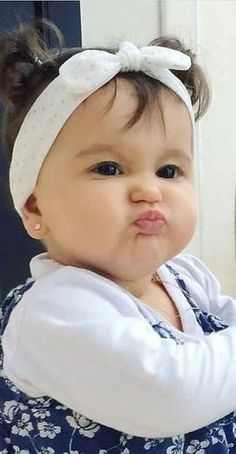 a baby girl wearing a white headband and looking at the camera