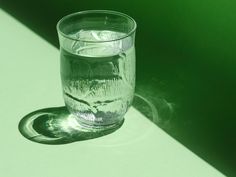 a clear glass sitting on top of a table next to a shadow from the sun