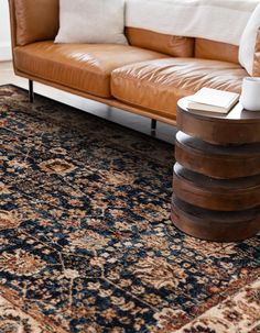 a brown leather couch sitting on top of a blue rug next to a wooden table