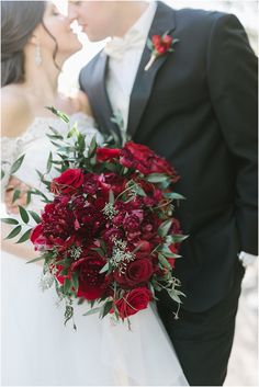 the bride and groom are kissing in front of each other with red flowers on their bouquet