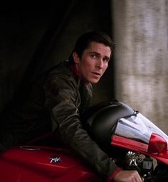 a man sitting on the back of a red motorcycle with his hand on the seat