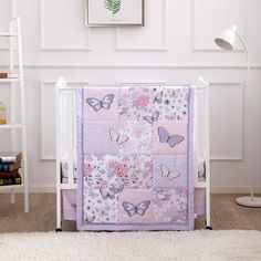 a baby crib with a pink and white butterfly quilt on the top, next to a book shelf