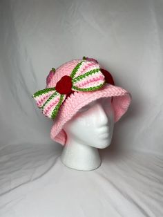 a white mannequin head wearing a pink hat with green and red trims