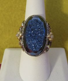 A Gorgeous Barbara Bixby Sterling Silver 18 Karat Gold Highlight Blue Oval Drussy Gemstone Ring - (Size 8). Visit this shop for a wide variety of Vintage Quality Jewelry, Art, Photos and Collectibles. ~Age (approximate): 1980's ~Material(s): Sterling Silver/18 Karat Gold Highlight/Blue Oval Drussy Gemstone ~Approx. Size: 8   ~Approx. Weight: N/A ~Signature / Brand: Unsigned. ~Condition: Excellent. Marked Bixby. ~International Shipping: Is Available, please contact us for a quote. ~Inventory #: 8993 Barbara Bixby Rings, Antique Hallmarked Sterling Silver Topaz Ring, Sterling Silver Multi-stone Jewelry With Oval Cabochon, Gold Highlight, Luxury Sterling Silver Sapphire-colored Topaz Ring, Luxury Sapphire-colored Topaz Ring In Sterling Silver, Bohemian Blue Oval Beads, Gems, And Cabochons, Gold Highlights, Art Photos