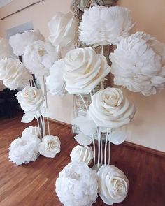 white paper flowers in vases on wooden floor next to wall with mirror behind them