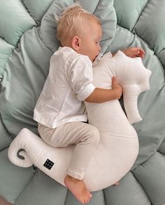 a baby laying on top of a white stuffed animal in a room with blue pillows