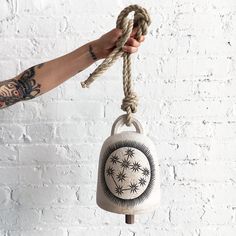 a hand holding a rope with a small bell hanging from it's end on a white brick wall