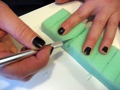 two hands with black and white manicures on their nails, one holding a green sponge