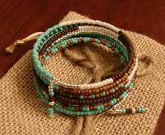 three bracelets with beads and feathers on top of a burlocked cloth